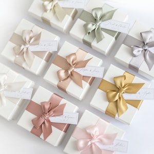 Personalised white favour boxes with ivory, taupe, hint of green, rose gold, cappuccino, sage green, powder pink, gold and silver/grey ribbon on top.