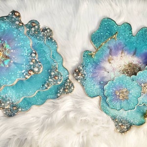 Op de afbeelding: Drie-laags turquoiseblauwe hars serveerplateau met een gouden standaard en parel accenten. Het plateau heeft een unieke, organische vorm en is perfect om desserts, hapjes of andere lekkernijen te presenteren.