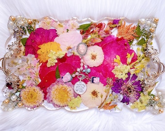 May include: A decorative resin tray filled with dried flowers in shades of pink, yellow, and purple. The tray has ornate silver handles and is embellished with pearls. A pendant with the text "Nothing is worth more" is visible.