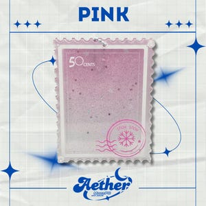 May include: A pink, stamp-shaped accessory with the word "PINK" at the top. The stamp features the text "50 cents" and a "SNOW SNOW" design with a snowflake. The brand "Aether" is at the bottom.