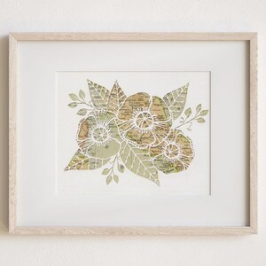 May include: A framed print of a floral design created with cut paper. The flowers are white and the leaves are green. The paper has a vintage map pattern.