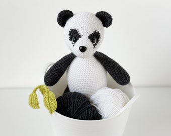 Puede incluir: Un juguete de panda blanco de crochet con ojos y orejas negros se sienta en un cubo de plástico blanco con hilo negro y blanco.