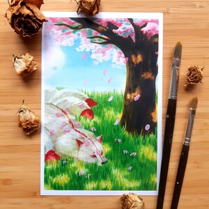Könnte beinhalten: Aquarellmalerei eines weißen Fuchses mit roten Markierungen, der sich im grünen Gras unter einem Kirschblütenbaum ausruht. Rosa Blütenblätter fallen vom Baum. Der Hintergrund ist ein blauer Himmel. Zwei Pinsel befinden sich rechts.