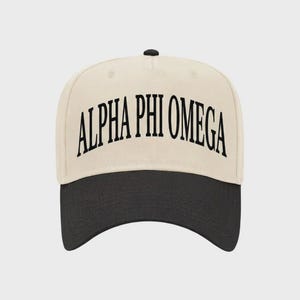 May include: A baseball cap with a cream-colored crown and a black brim. The front of the crown features the text ALPHA PHI OMEGA in a bold, black, arched serif font. The cap has a small black button at the top center of the crown.