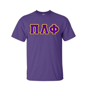 May include: A purple t-shirt with the Greek letters ΠΛΦ in yellow with a gold outline. The letters are centered on the front of the shirt. The shirt has short sleeves and a crew neck.