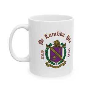 May include: A white ceramic mug featuring the Pi Lambda Phi fraternity crest in purple, green, and gold. The design includes a lion, a lamp, and the text Pi Lambda Phi 1895, along with the Greek letters ΦΛΦ and the motto Nostros Amemus on a banner.