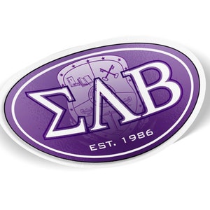 May include: An oval sticker with a purple and white design. The sticker features the Greek letters ΣΛB, a crest with keys and a book, and the text "EST. 1986". The sticker has a white border and a slight shadow.