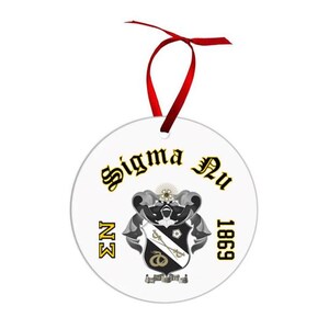 May include: A white, round ornament with the words "Sigma Nu" in gold script. The ornament features a black and white crest with a red ribbon for hanging. The year "1869" is printed in black.