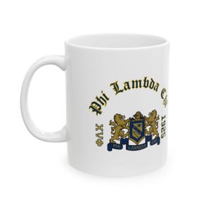 May include: A white ceramic mug featuring the Phi Lambda Chi fraternity crest in blue and gold. The design includes two lions flanking a central shield, the text Phi Lambda Chi, the year 1925, and Greek letters arranged in a circular pattern.