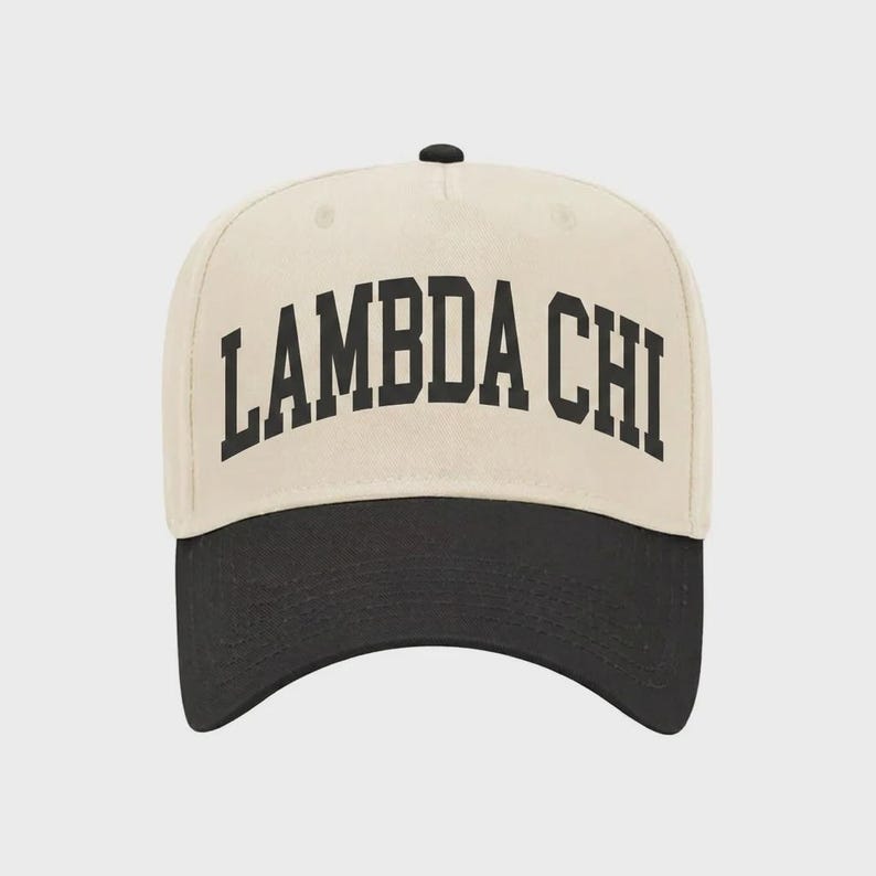 Pu&ograve; includere: Un cappellino da baseball color crema con visiera nera e un bottone nero sulla parte superiore. La parte anteriore del cappellino presenta il testo LAMBDA CHI in un carattere serif nero, in grassetto e arcuato. Il cappellino ha una corona strutturata.