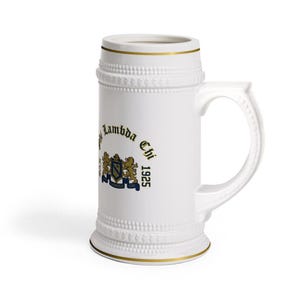 May include: A white ceramic beer stein featuring a gold-trimmed rim and base, with a textured beaded band near the top and bottom. The front displays a blue and gold crest with two lions, the text Phi Lambda Chi, and the year 1925 in black.