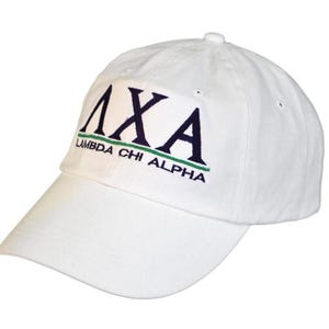 May include: A white baseball cap with a curved brim. The cap features the Greek letters ΛXA in navy blue, with the words "LAMBDA CHI ALPHA" embroidered in navy blue and green. The cap is made of a soft fabric.
