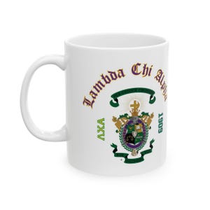 May include: A white ceramic mug featuring the Lambda Chi Alpha fraternity crest in purple, green, and gold. The text reads Lambda Chi Alpha, AXA, and 1909, with the Latin motto Per Crucem Crescens and Vir Quisque Vir Quisque printed on green ribbons.