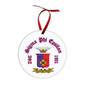 May include: A white, round ornament with a red ribbon for hanging. The ornament features the text "Sigma Phi Epsilon" in purple script, along with a crest design in red, purple, and gold. The year "1901" is also displayed.