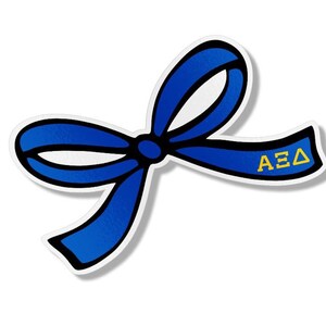 May include: A blue ribbon sticker with a black outline and the Greek letters ΑΞΔ in yellow. The sticker has a white background and a shadow effect, giving it a 3D appearance. The ribbon is tied in a bow.