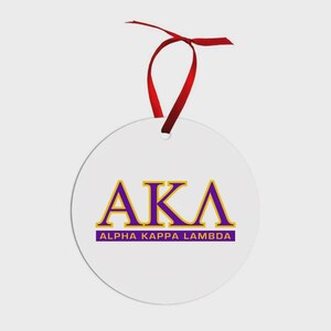 May include: A circular white ornament featuring the purple and gold Greek letters AKA with the text ALPHA KAPPA LAMBDA printed in purple and gold below. The ornament is suspended by a thin red ribbon tied in a bow at the top of the piece.