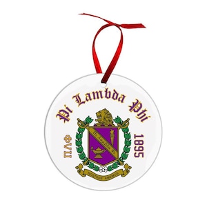 May include: A white, round ornament with a red ribbon. The ornament features a crest with the words "Pi Lambda Phi" in gold lettering. The crest includes a lion, a lamp, and the year 1895.