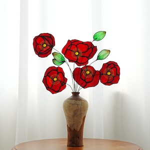 May include: A bouquet of red poppies with green leaves in a brown ceramic vase on a wooden table.