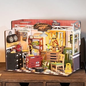 Könnte beinhalten: Ein Miniaturmodell aus Holz einer Garagenwerkstatt mit einer roten Werkzeugkiste, einem schwarzen Werkzeugschrank, einer Holzwerkbank und einem Schild mit der Aufschrift "Garage".