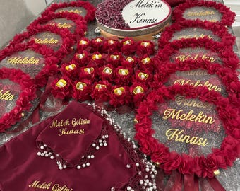 Puede incluir: Un conjunto de artículos decorativos rojos y dorados para una ceremonia de boda. Los artículos incluyen una cesta, un pandero, una bandeja y varias cajas pequeñas rojas y doradas. Los artículos están decorados con flores y el texto "Melek'in Kinası" y "Melek Gelinin Kınası".