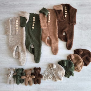 May include: Set of six knitted baby outfits in brown, green, and beige. The outfits include long-sleeved onesies and matching hats. The hats have bear ears.