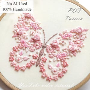 May include: An embroidered butterfly design on a hoop, featuring pink and white floral patterns. The text "No AI Used 100% Handmade" and "PDF Pattern" are visible. The words "YouTube video tutorial" are also visible. The embroidery is handmade.