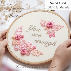 May include: Hand-embroidered hoop art with the phrase "You are enough" in cursive script. The design features pink and peach floral embroidery. The text "PDF Pattern" and "You Tube video tutorial" are also visible.