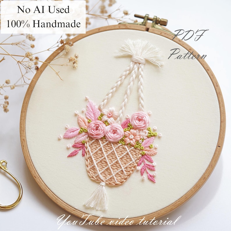 May include: Hand-stitched embroidery in a wooden hoop. The design features a hanging basket filled with pink roses and greenery. The text "No AI Used 100% Handmade" and "PDF Pattern" are visible. The words "YouTube video tutorial" are also present.