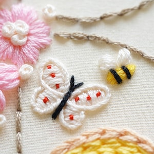 May include: Detailed embroidery showing a white butterfly with red spots and black antennae, a yellow and black bee, and pink flowers. The design is on cream fabric, with brown thread details.