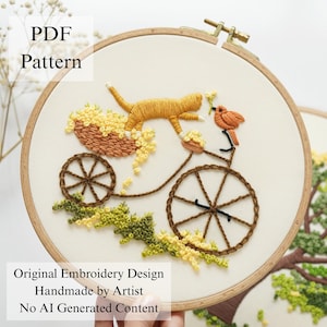 Pu&ograve; includere: Un telaio da ricamo circolare in legno contenente un pannello in tessuto con un disegno cucito a mano di un gatto arancione su una bicicletta con un cesto di fiori gialli e un piccolo uccellino arancione. Il testo PDF Pattern, Original Embroidery Design, Handmade by Artist, No AI Generated Content &egrave; visibile.