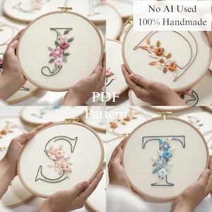 Op de afbeelding: Handgeborduurde bloemenletters in houten hoepels. Elke hoepel heeft een andere letter, zoals J, D, S en T, versierd met kleurrijke bloemborduurwerk. De tekst "No AI Used 100% Handmade" en "PDF Pattern" is ook zichtbaar.