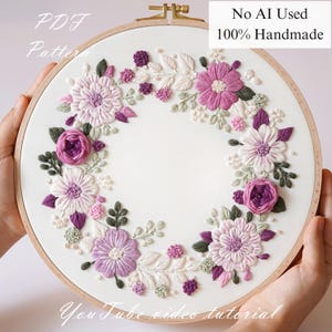 Peut inclure: Un cercle à broder fait à la main avec une couronne florale. La couronne comprend des fleurs violettes, roses et blanches avec des feuilles vertes, le tout brodé sur du tissu blanc. Le texte "No AI Used 100% Handmade" est visible.