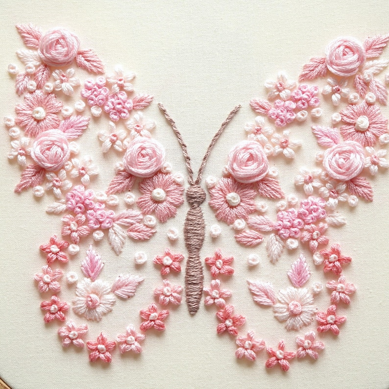May include: A detailed embroidery of a butterfly, created with pink and white thread. The wings are formed from various flowers, including roses, and the body is a textured brown. The background is a cream colour, highlighting the intricate floral design.