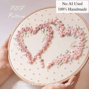 May include: Hand-embroidered floral design in a wooden hoop. The artwork features two heart shapes formed by pink roses and green leaves on a cream-colored fabric. The text "PDF Pattern" and "No AI Used 100% Handmade" are visible.