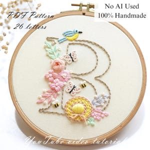 May include: Embroidered letter "B" in a wooden hoop, decorated with flowers, butterflies, and a bird. The design features pink flowers and insects. Text on the hoop reads "PDF Pattern 26 letters" and "No AI Used 100% Handmade".