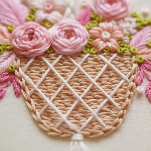May include: Embroidered floral basket design featuring pink roses, peach-colored flowers, and green accents. The basket is a light peach color with a white crisscross pattern. The embroidery is detailed and textured.
