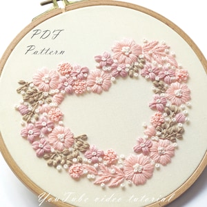 May include: A PDF pattern for a floral embroidery hoop art project. The design features a heart shape made of pink and brown flowers and leaves.