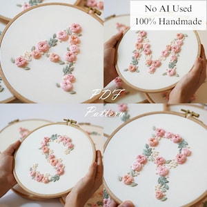 Op de afbeelding: Handgeborduurde borduurringen met de letters A, M, S en R. Elke letter is gemaakt met roze en perzikrozen, groene bladeren en witte accenten op een witte stoffen achtergrond. De tekst "No AI Used 100% Handmade" is zichtbaar.
