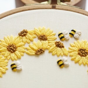 May include: Hand-stitched embroidery of yellow sunflowers with brown centres and tiny bees in a wooden hoop. The design showcases a floral theme, with a focus on the handcrafted nature of the piece.