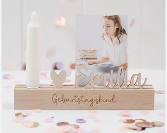May include: Wooden photo frame with a candle holder, a heart cutout, and the name "Emilia" engraved on it. The frame also has the text "Geburtstagskind" engraved on it. The frame is sitting on a table with confetti.