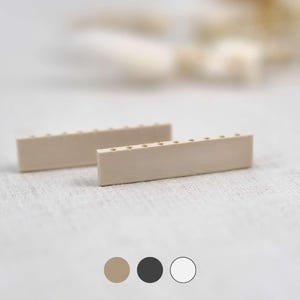 Könnte beinhalten: Zwei rechteckige, hellbeige Holzblöcke mit gleichmäßig verteilten Löchern entlang einer Kante. Die Blöcke sind auf einem neutralen Hintergrund positioniert, was auf ein Bastel- oder DIY-Projekt hindeutet. Das Bild enthält auch Farbmuster.