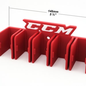Puede incluir: Porta palos de hockey de pl&aacute;stico rojo con el logotipo de CCM en blanco. El porta palos tiene seis ranuras para palos y mide 14,6 cm de ancho y 4 cm de alto.