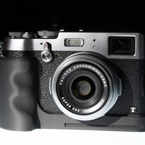 May include: A silver and black digital camera with a black lens and a black grip. The camera has a black strap attached to it.