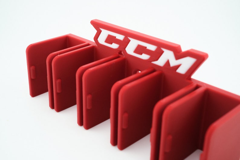 Puede incluir: Porta palos de hockey de pl&aacute;stico rojo con seis ranuras y el logotipo de CCM en blanco.