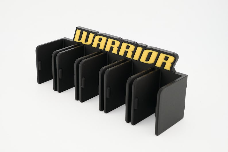 Puede incluir: Organizador de pl&aacute;stico negro con ranuras para guardar objetos. El organizador tiene la palabra "WARRIOR" impresa en amarillo en la parte superior.