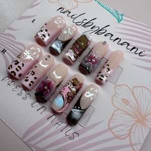 Pu&ograve; includere: Un set di dieci unghie press-on con vari design. Le unghie sono nude con fiori bianchi, stampa leopardata e orsetti dei cartoni animati. La carta recita "nailshopbanani" e "press on nails".