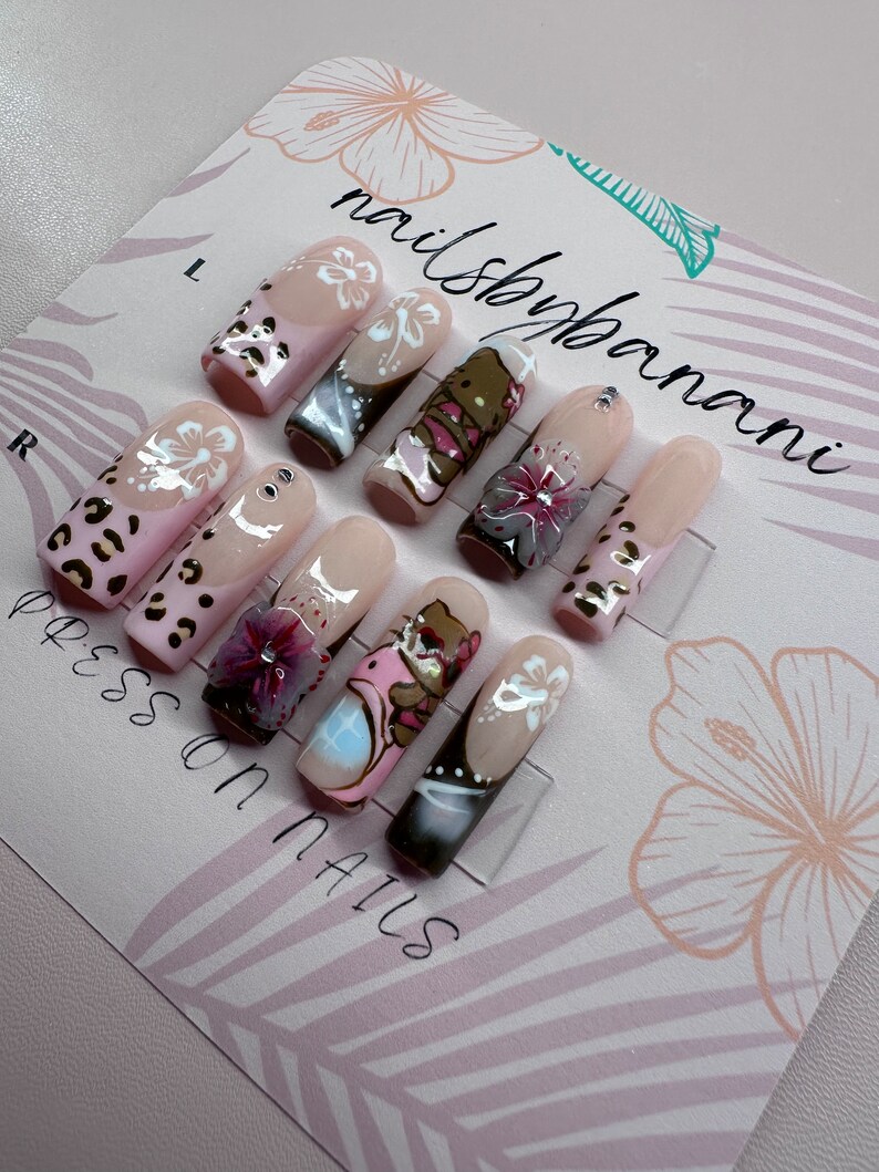 Pu&ograve; includere: Un set di dieci unghie press-on con vari design. Le unghie sono nude con fiori bianchi, stampa leopardata e orsetti dei cartoni animati. La carta recita "nailshopbanani" e "press on nails".