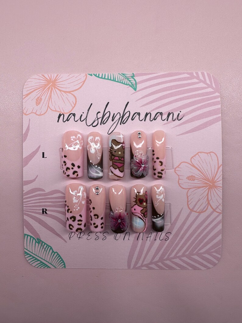Pu&ograve; includere: Un set di 10 unghie finte con base rosa e vari design, tra cui un personaggio di Hello Kitty, fiori e stampa leopardata. Le unghie sono esposte su una carta rosa con il testo "nailsbybanani" e "PRESS ON NAILS".