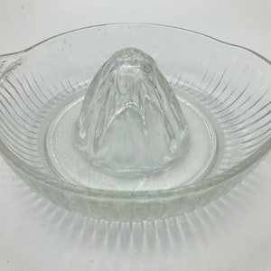 Puede incluir: Exprimidor de cítricos de vidrio transparente con un cuenco acanalado y un escariador central. El exprimidor tiene un asa y un pico vertedor. Una herramienta de cocina para exprimir zumo fresco.