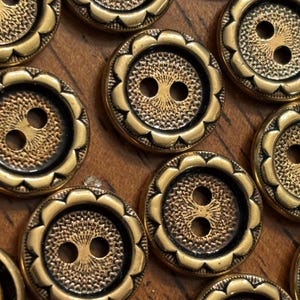 May include: Close-up of several antique gold-colored buttons. Each button has a scalloped edge and a detailed center design with two holes for sewing. The buttons are arranged on a wooden surface.